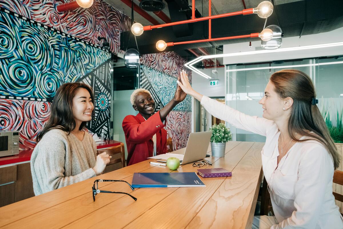 Três mulheres em posição de liderança comemorando em área comum da empresa